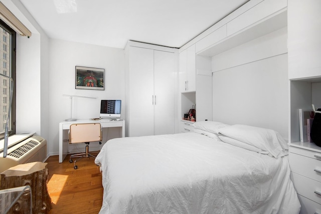 bedroom with an AC wall unit, light wood-style floors, and a closet