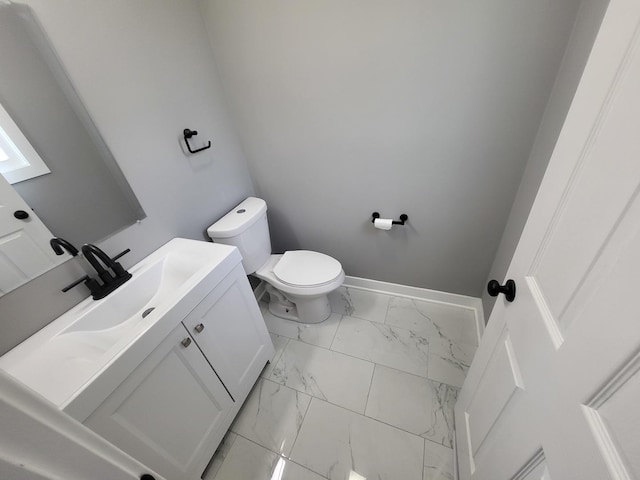 half bathroom featuring toilet, marble finish floor, baseboards, and vanity