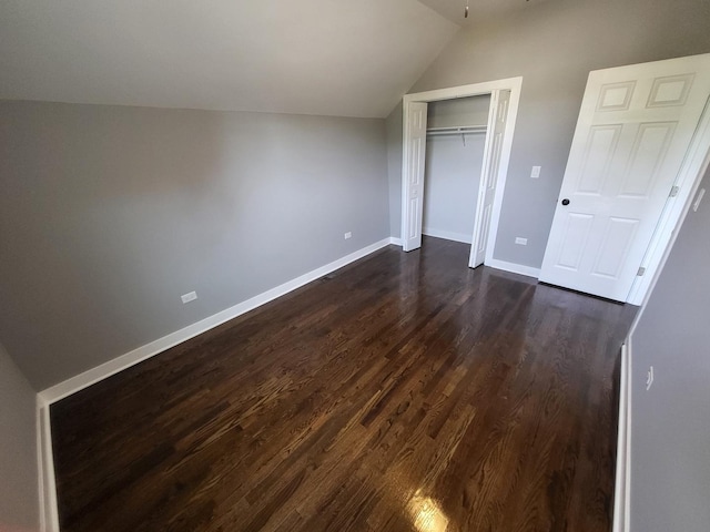unfurnished bedroom with lofted ceiling, a closet, dark wood finished floors, and baseboards