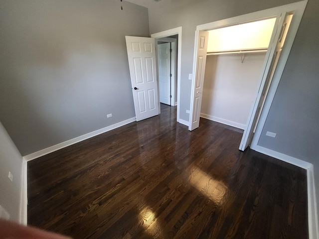 unfurnished bedroom featuring dark wood-style floors, a closet, and baseboards
