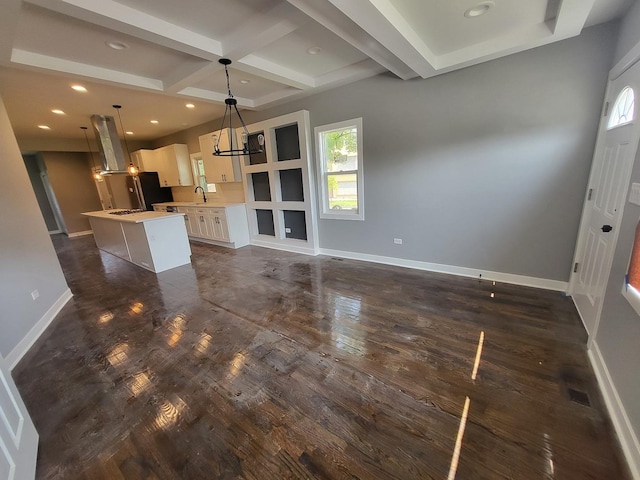 unfurnished living room featuring baseboards, dark wood finished floors, coffered ceiling, a sink, and beam ceiling