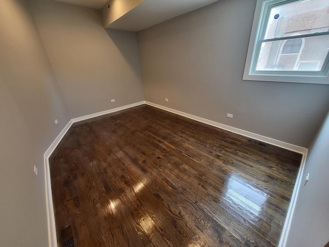 spare room featuring dark wood-type flooring, visible vents, and baseboards