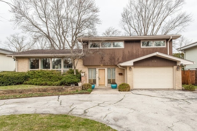 view of front facade with driveway, an attached garage, fence, and brick siding