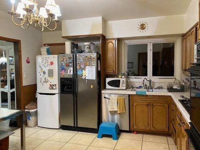 kitchen with tile countertops, white microwave, a sink, fridge with ice dispenser, and dishwasher