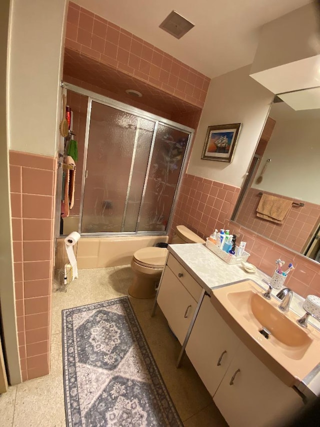 bathroom with wainscoting, toilet, combined bath / shower with glass door, vanity, and tile walls