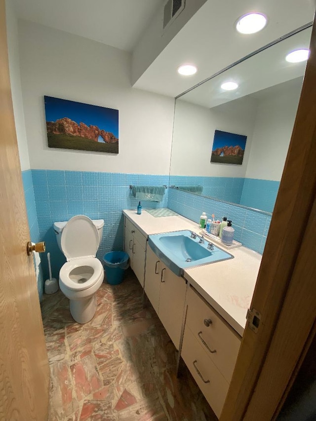 bathroom with visible vents, wainscoting, toilet, vanity, and tile walls