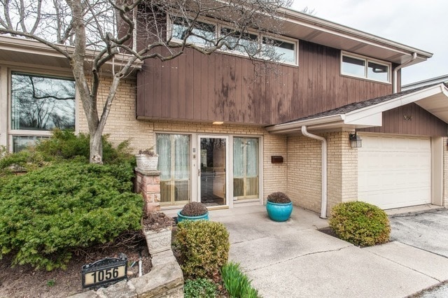 view of exterior entry featuring a garage, brick siding, and aphalt driveway