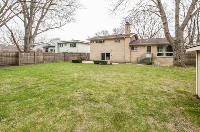 back of property featuring a fenced backyard, a chimney, and a yard