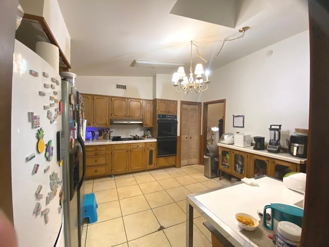 kitchen with light tile patterned floors, under cabinet range hood, light countertops, brown cabinets, and black appliances