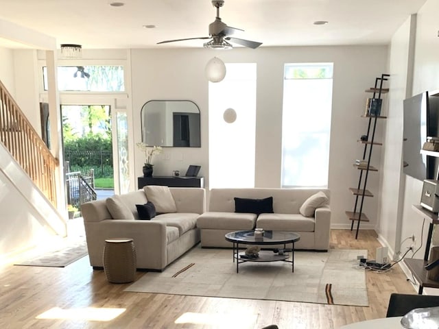 living area featuring ceiling fan, baseboards, light wood-style flooring, and stairs