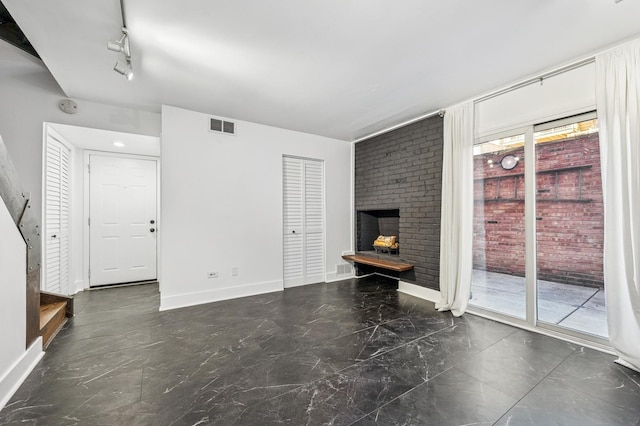 unfurnished living room with track lighting, a fireplace, visible vents, and baseboards