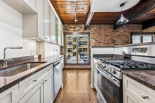 kitchen with beam ceiling, a sink, stainless steel appliances, wooden ceiling, and brick wall