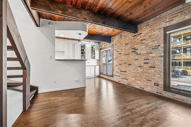 unfurnished living room featuring brick wall, stairway, wood ceiling, beam ceiling, and dark wood-style flooring