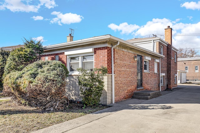 view of side of property with driveway, brick siding, and a chimney