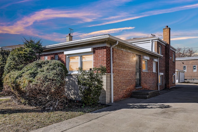 view of home's exterior featuring driveway, brick siding, and a chimney