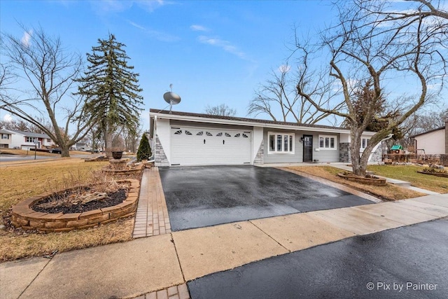 ranch-style home featuring an attached garage, a front lawn, and aphalt driveway