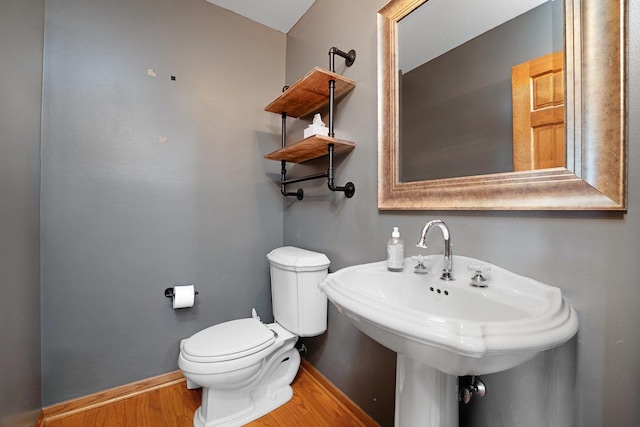 half bath with baseboards, toilet, and wood finished floors