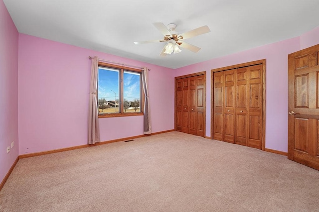 unfurnished bedroom with visible vents, baseboards, multiple closets, light carpet, and a ceiling fan