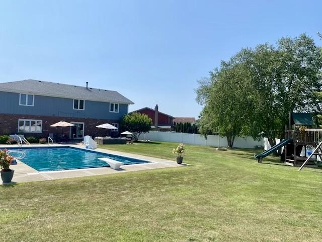 view of swimming pool featuring a fenced in pool, playground community, a fenced backyard, a diving board, and a lawn