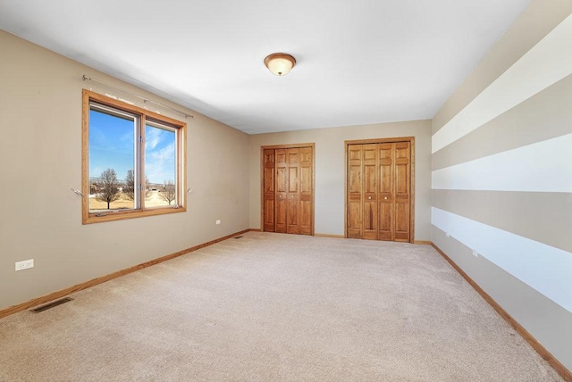 unfurnished bedroom with visible vents, two closets, baseboards, and carpet floors