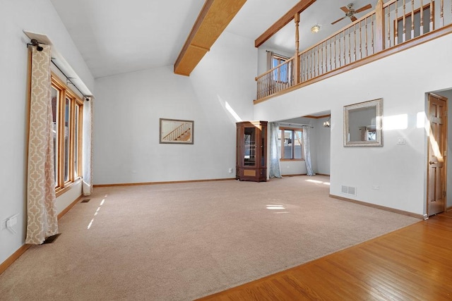 unfurnished living room featuring carpet, baseboards, visible vents, high vaulted ceiling, and beam ceiling