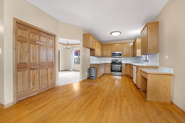 kitchen with baseboards, light wood-type flooring, light countertops, appliances with stainless steel finishes, and a sink