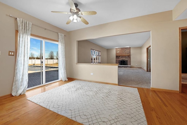 living room featuring ceiling fan, baseboards, a brick fireplace, and wood finished floors