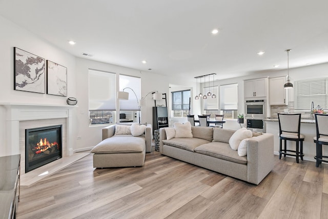 living area featuring a glass covered fireplace, recessed lighting, visible vents, and light wood finished floors