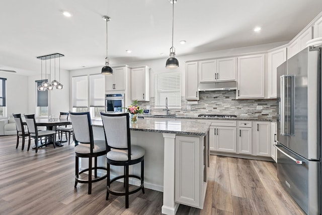 kitchen featuring a sink, under cabinet range hood, a center island, stainless steel appliances, and white cabinets