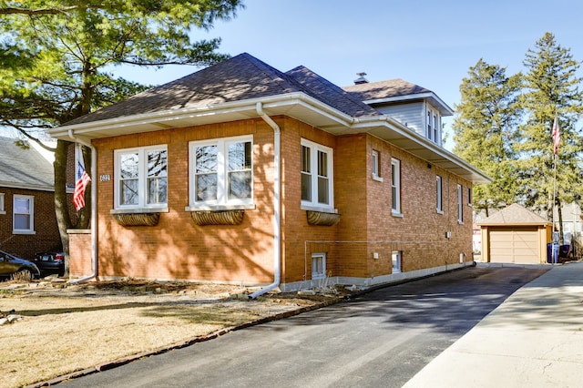 view of side of home with brick siding, a shingled roof, aphalt driveway, a garage, and an outdoor structure