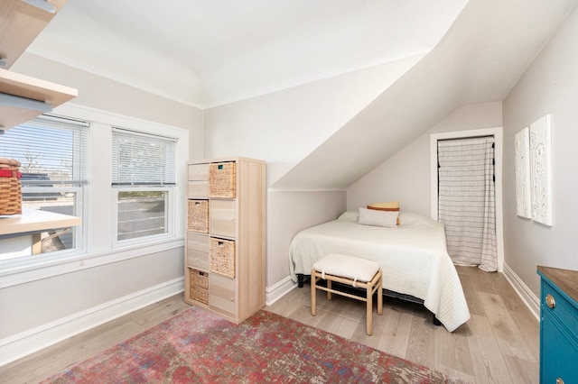 bedroom with baseboards, vaulted ceiling, and light wood finished floors