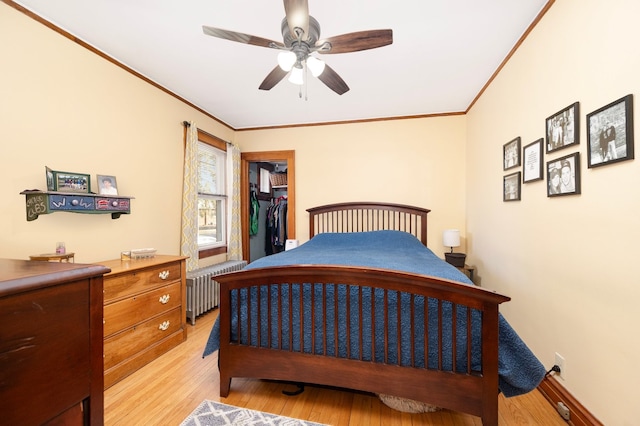 bedroom featuring radiator heating unit, ceiling fan, light wood-style floors, a walk in closet, and crown molding