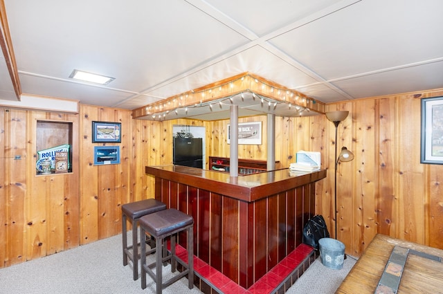 bar featuring wooden walls, a bar, freestanding refrigerator, and carpet