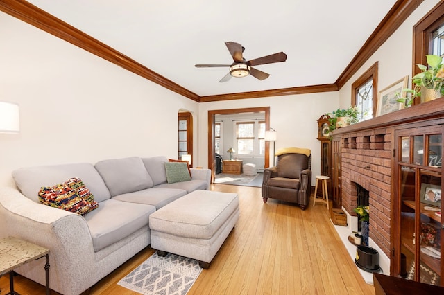 living area featuring a brick fireplace, light wood-style floors, a healthy amount of sunlight, and crown molding