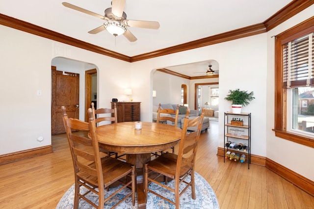 dining space with ceiling fan, baseboards, ornamental molding, light wood-style flooring, and arched walkways