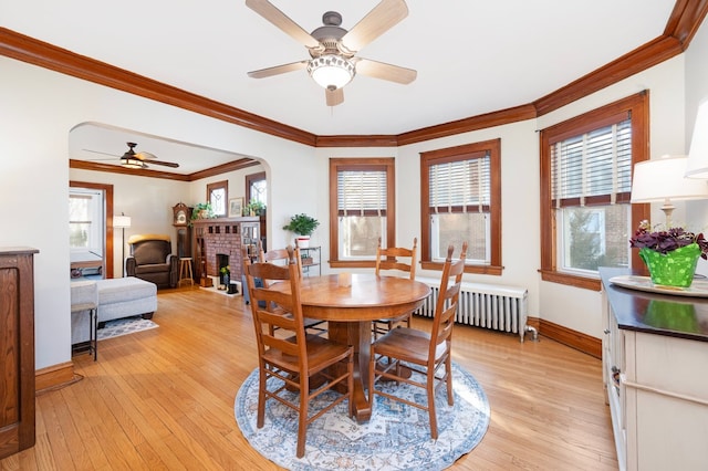 dining room with light wood-style floors, radiator, a fireplace, and arched walkways