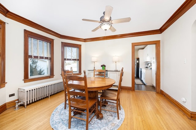 dining room featuring baseboards, radiator heating unit, arched walkways, ornamental molding, and light wood-style floors