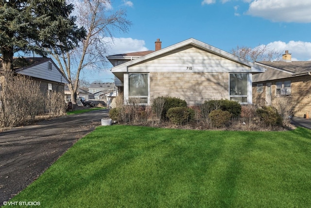 exterior space featuring aphalt driveway, a front yard, and a chimney