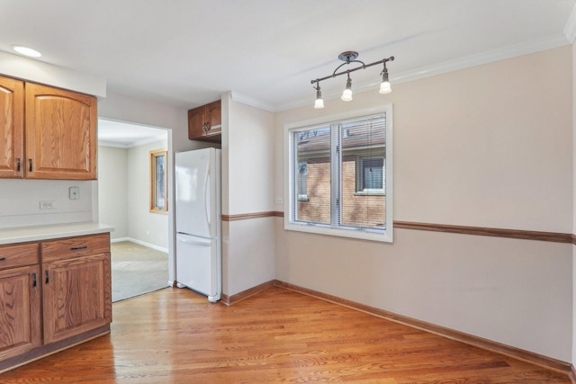 kitchen with baseboards, light wood finished floors, freestanding refrigerator, light countertops, and crown molding