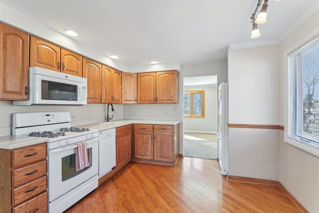 kitchen with baseboards, light countertops, light wood-style flooring, brown cabinets, and white appliances