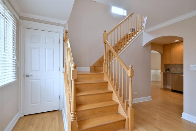 staircase with arched walkways, wood finished floors, baseboards, and ornamental molding