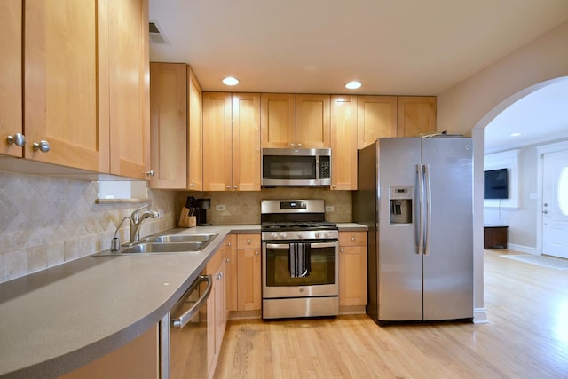 kitchen with light wood-type flooring, light brown cabinetry, a sink, appliances with stainless steel finishes, and decorative backsplash