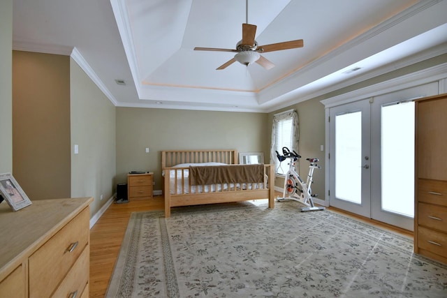 bedroom with light wood-type flooring, visible vents, a tray ceiling, french doors, and crown molding