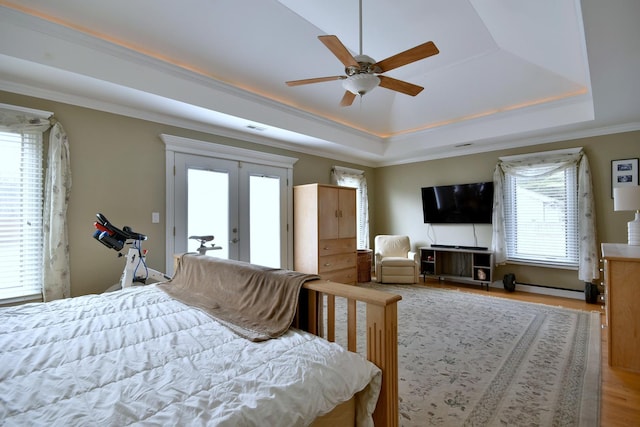 bedroom featuring a raised ceiling, wood finished floors, french doors, and ornamental molding