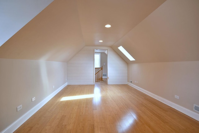 additional living space featuring light wood finished floors, visible vents, vaulted ceiling with skylight, and baseboards