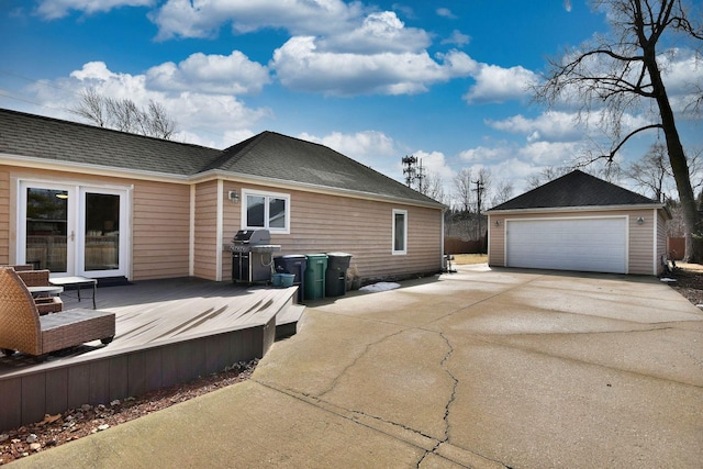 back of house with an outbuilding, roof with shingles, a detached garage, and a wooden deck