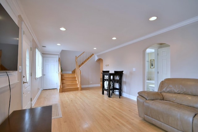 interior space with light wood finished floors, crown molding, baseboards, stairs, and arched walkways