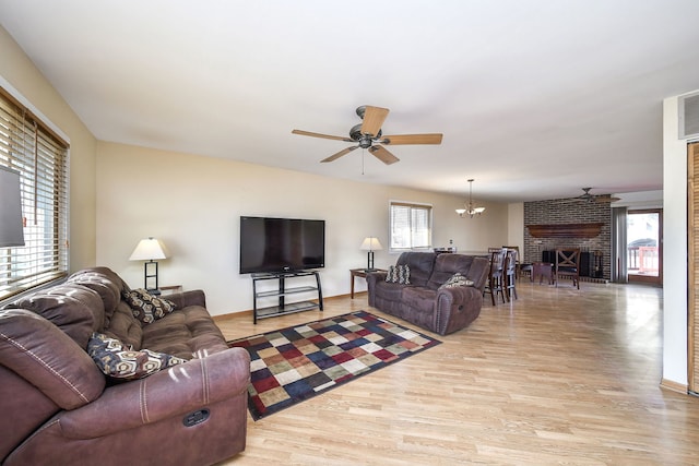 living area with ceiling fan with notable chandelier, light wood-style floors, baseboards, and a fireplace