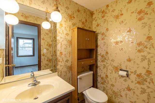 half bathroom featuring vanity, toilet, and wallpapered walls