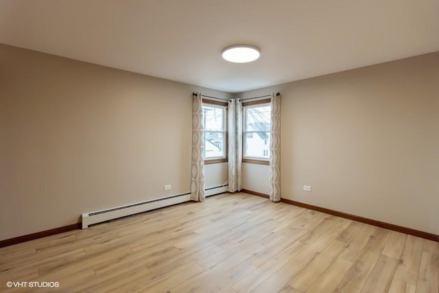 empty room with a baseboard heating unit, light wood-style floors, and baseboards